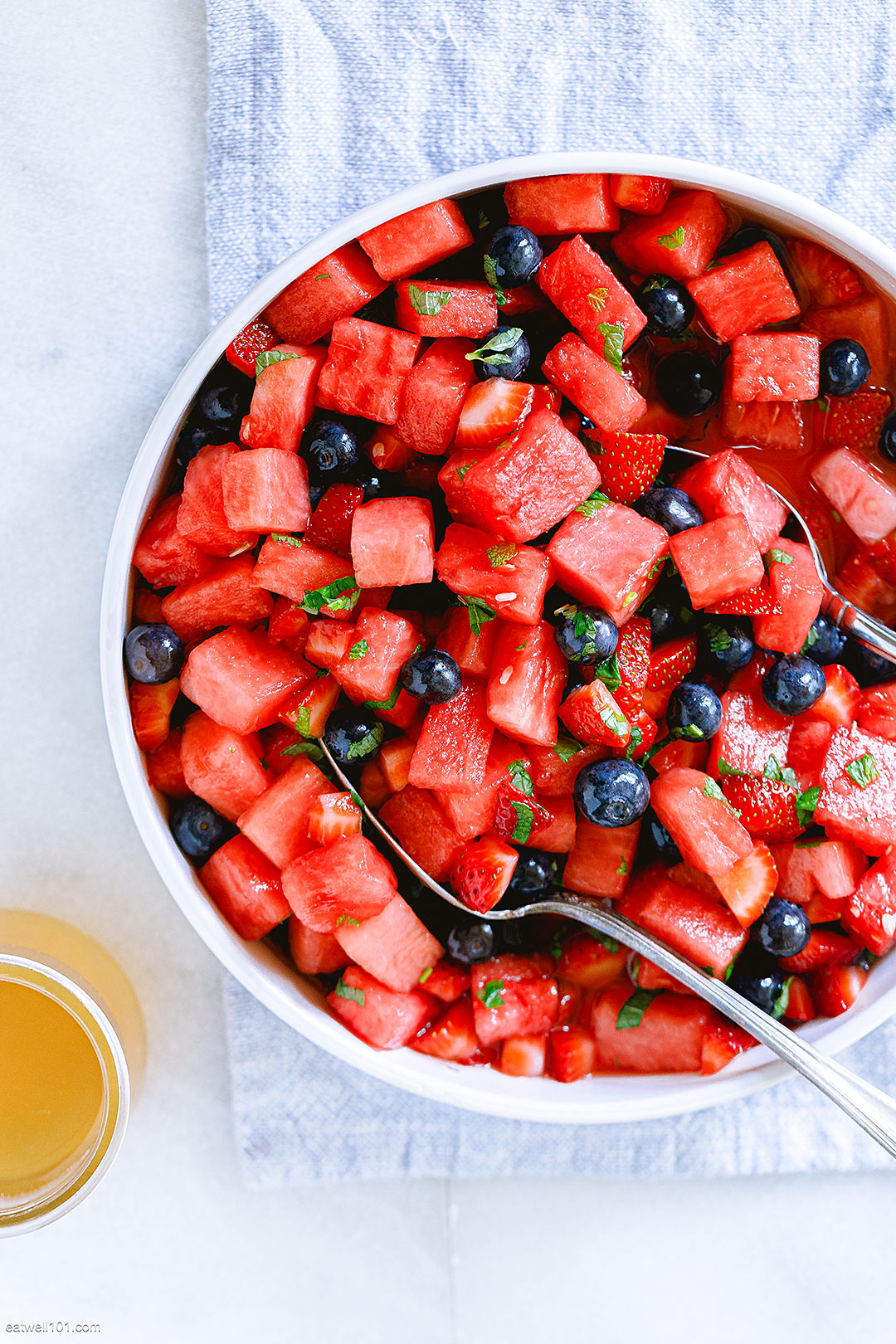 Variety of summer salads on a table, including summer pasta salad, summer fruit salad, and a leafy green summer salad with fresh strawberries.